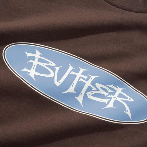 Light blue oval logo with white stylized lettering reading BUTTER on a brown fabric t-shirt.