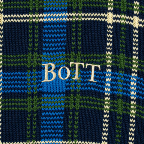 Close-up of a navy, blue, green, and cream tartan knit fabric with the word "BOTT" embroidered in cream letters across the center.