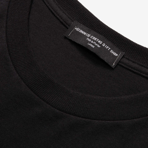 Close-up of the crew neck and inside label of a black t-shirt, with a printed tag reading "CONNIE COST4S GIFT SHOP" and "LARGE".