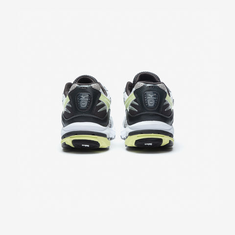 Rear view of a pair of white, black and pale yellow-green running shoes on a plain light background.