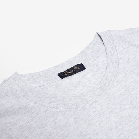 Close-up of the crew neckline of a heather grey t-shirt, with a navy woven label reading "Dime Mtl" in gold script.