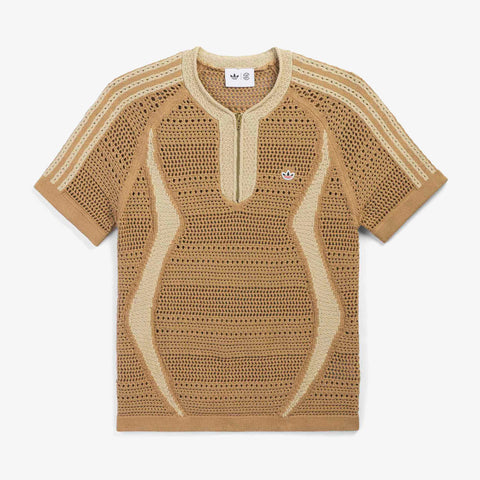 Short-sleeved tan knit top with an open-weave crochet pattern, wavy lighter stripes, a zip-neck placket, and a small logo on the chest.