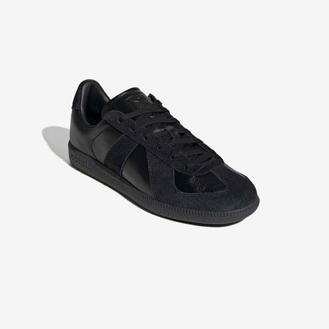 Black low-top sneaker shown at a three-quarter angle, with smooth leather upper, suede panels, black laces, and a black rubber sole.