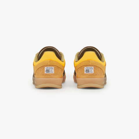 Rear view of a pair of yellow and tan low-top sneakers with brown suede heel panels and a gum rubber sole, shown on a white background.