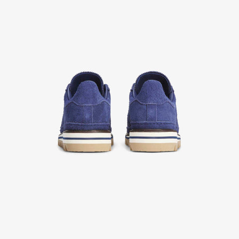 Rear view of a pair of navy blue suede low-top sneakers with tan and white rubber soles on a white background.