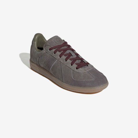 Grey suede low-top sneaker with maroon laces, olive green heel tab, and gum rubber sole, shown at a three-quarter angle on a white background.