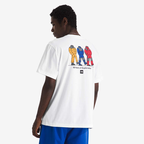 Back view of a white short-sleeve t-shirt with a print of three figures in colourful puffy suits walking, and the text "60 Years of Exploration".
