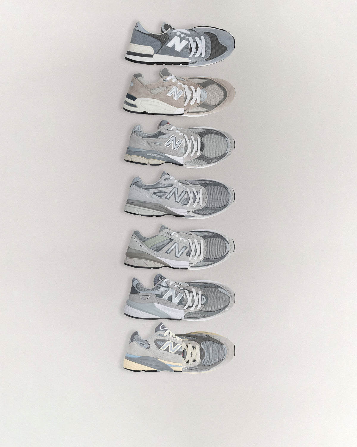Seven grey and silver running sneakers laid out in a vertical line on a light background, showing their side profiles with varied shades of grey.