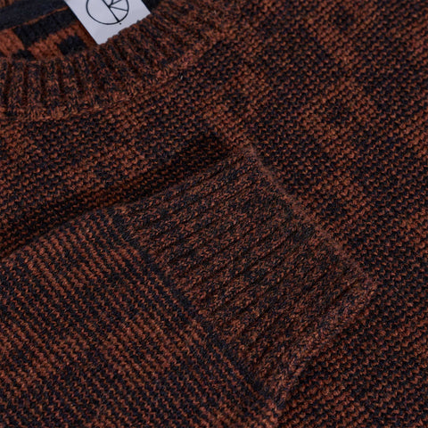 Close-up of a rust-brown and black knitted sweater with a ribbed crew neck and cuff, showing its marled textured knit pattern.