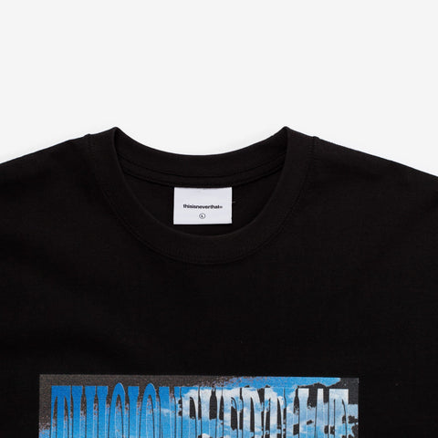 Close-up of a black crew-neck t-shirt collar with a white neck label, and a blue graphic print with stretched, distorted lettering on the chest.