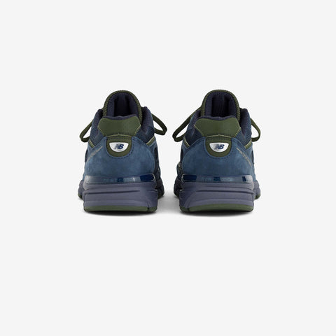 Rear view of a pair of navy blue suede running shoes with olive green heel accents and a white logo tab on the heel.