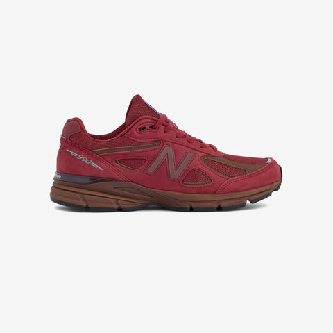 Side view of a red running shoe with a brown midsole and sole, a brown N logo on the side, and a silver 990 badge at the heel.
