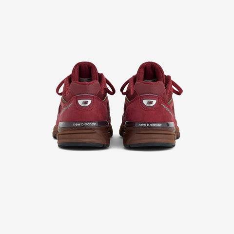 Rear view of a dark red New Balance sneaker with a brown midsole and sole, laces tied at the top, and the New Balance logo on the heel.