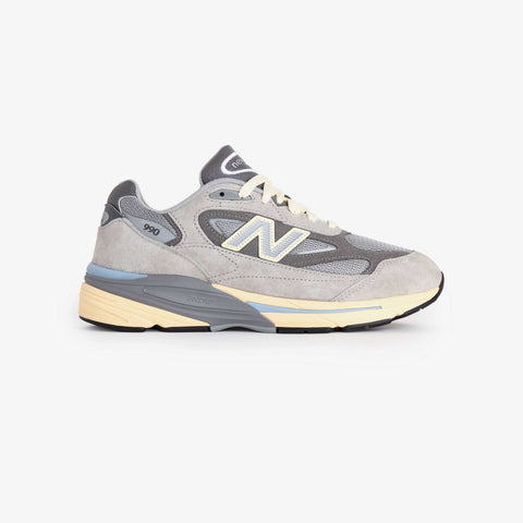 Grey running shoe with suede and mesh upper, cream laces, blue-grey midsole and a large white N logo on the side.