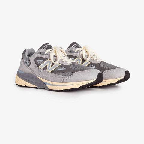 Pair of grey New Balance running sneakers with suede overlays, cream laces, and a cream and pale blue midsole, shown from the front three-quarter angle.