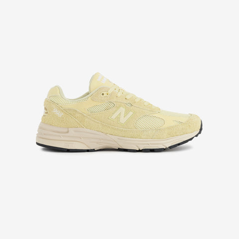 Pale yellow suede and mesh running shoe with a cream midsole and black outsole, shown in side profile against a white background.