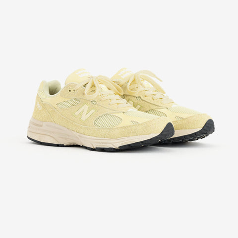 Pair of pale yellow running shoes with cream laces, suede and mesh panels, and a large white N logo on the side.