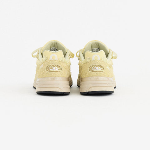 Rear view of a pale yellow suede sneaker pair with a white "USA" badge on each heel and a cream sole.