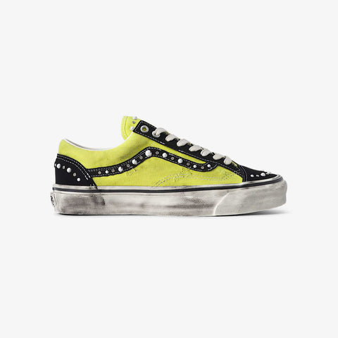Low-top sneaker with a bright yellow canvas upper, black suede toe and heel panels, white studded trim along the side, and a distressed white sole.