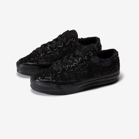 Pair of black low-top sneakers with a textured sequined upper, black laces, and black rubber soles, shown at an angle on a white background.