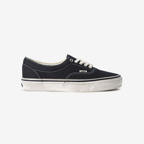 Black low-top canvas sneaker with white laces, white stitching, and a worn white rubber sole, shown from the side on a plain background.
