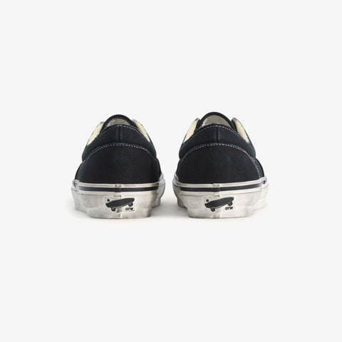 Rear view of a pair of black low-top canvas sneakers with white distressed soles and a small black logo on each heel.