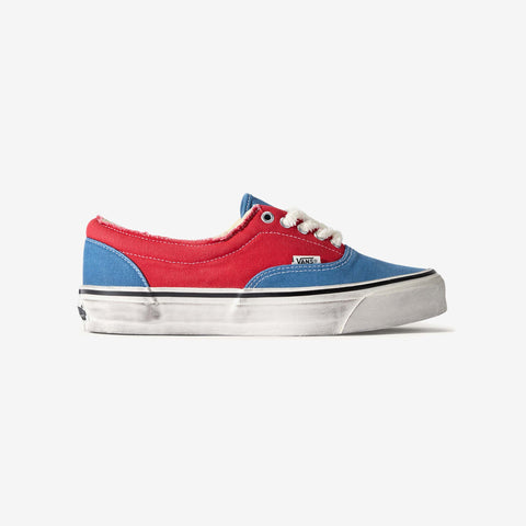 Red and blue low-top canvas sneaker with white laces and a worn white rubber sole, shown from the side on a white background.