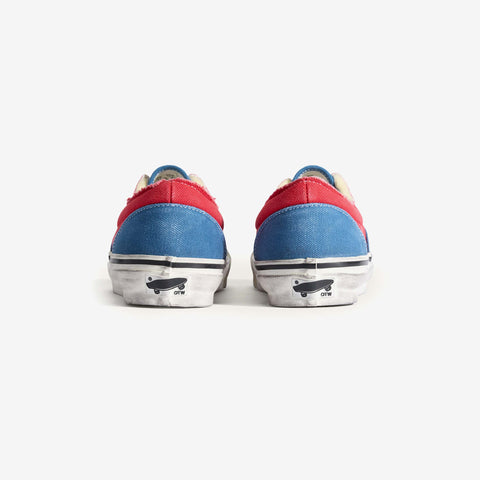 Rear view of a pair of low-top canvas sneakers with red and blue panels, distressed white midsoles, and a small skateboard logo on each heel.
